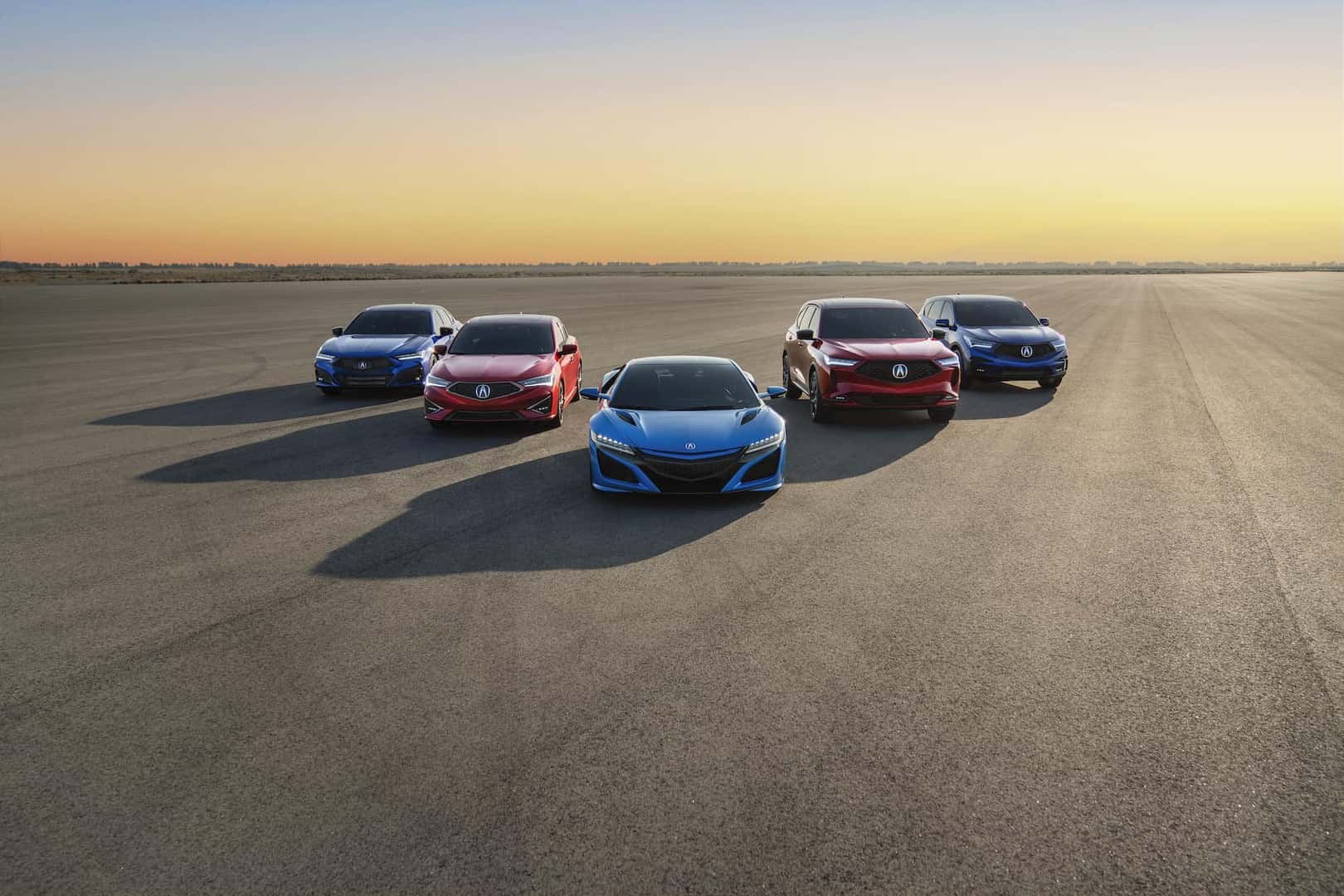 Acura family shot with blue and red colors and parked in front of a sunset.