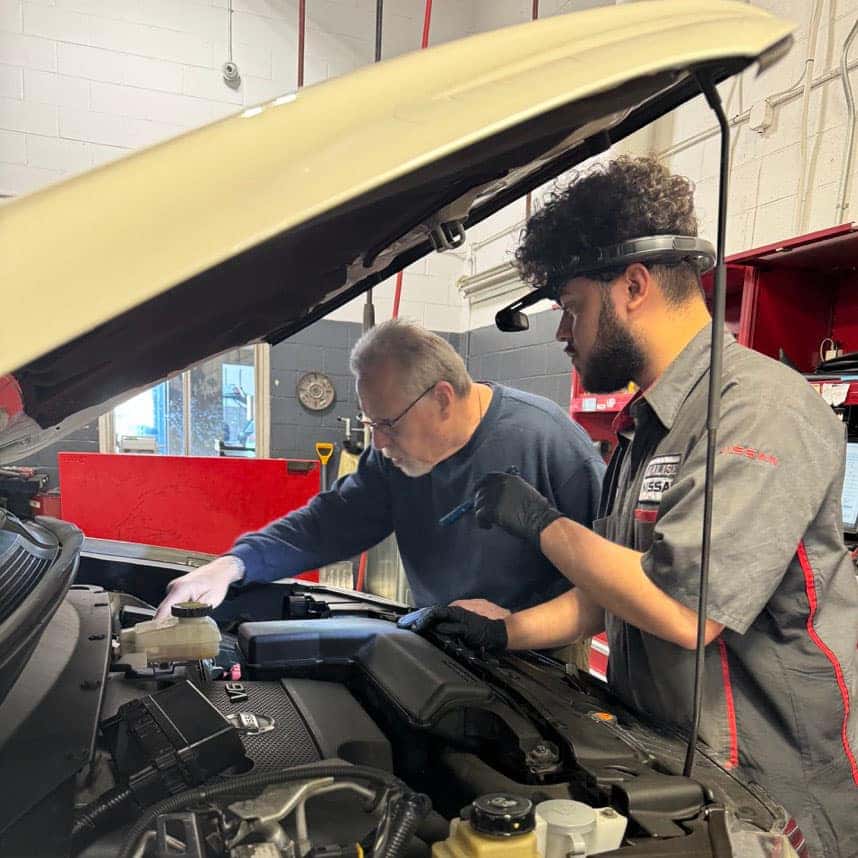 Nissan service technician wearing LenZ headset while inspecting the engine bay of a sedan