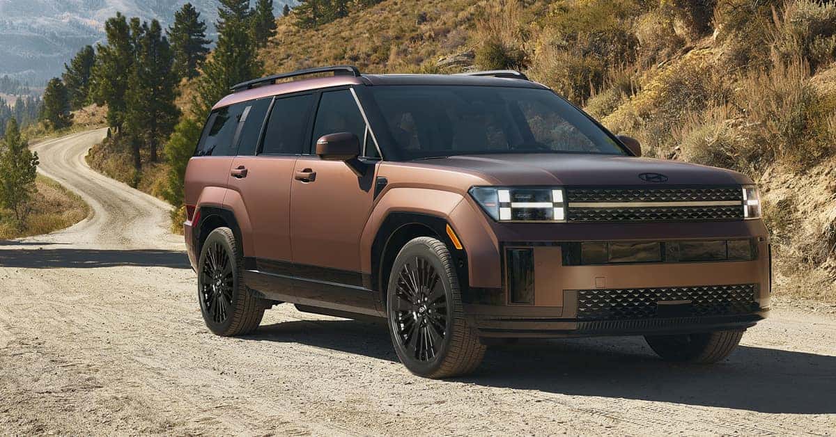 A matte brown SUV with black rims is parked on a dirt road .