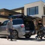 Family loading golf bags into the cargo area of a 2026 INFINITI QX80 parked in the driveway of a modern home, getting ready to leave for a golf outing