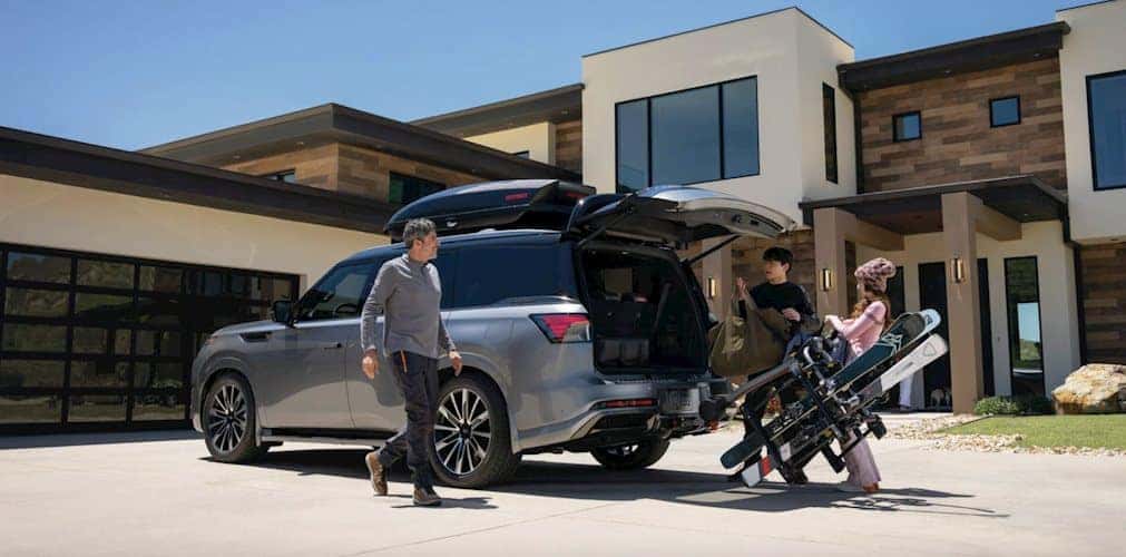 Family loading skis into the cargo area of a 2026 INFINITI QX80 parked in the driveway of a modern home, getting ready to leave for a ski outing