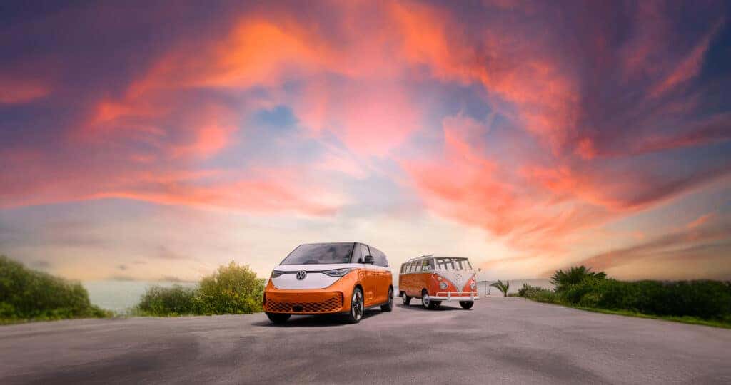 2025 VW ID BUZZ in metallic orange color next to an old VW Bus in orange near the ocean