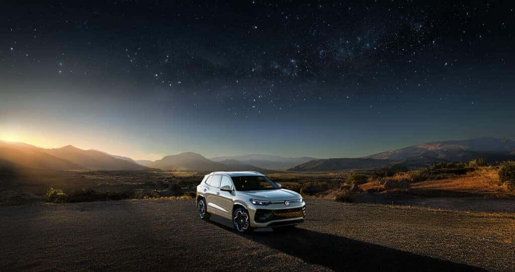 2025 Volkswagen Tiguan parked in a desert at sunset with mountains in the distance and stars in the sky