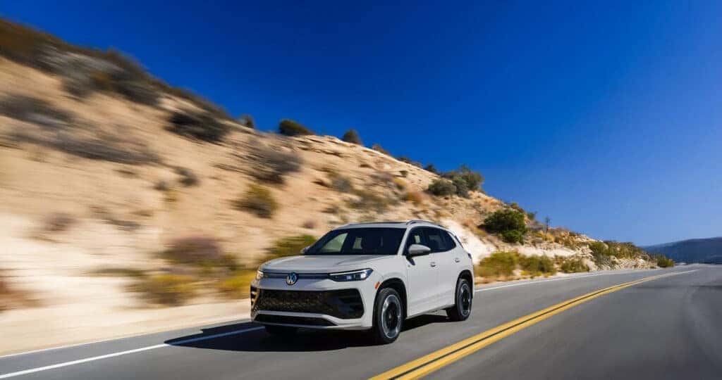 2025-VW-Tiguan-Driving-down-the-road-with-background-of-dry-land-and-trees-blurred