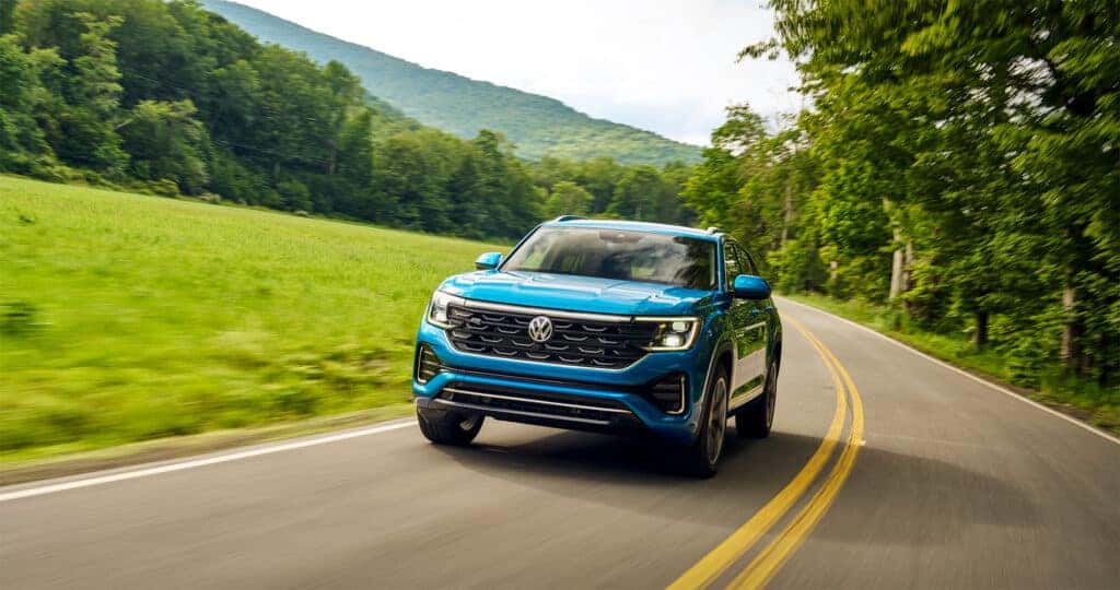 2026 Volkswagen Atlas performance being shown off while driving through vibrant green mountainscapes on a winding road