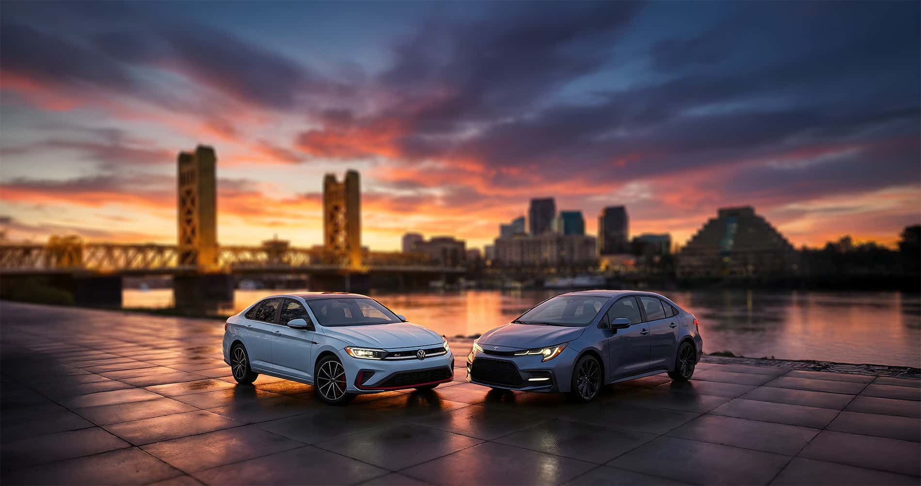 2026 Toyota Corolla vs Volkswagen Jetta parked on the Sacramento riverfront at sunset with tower bridge in the background