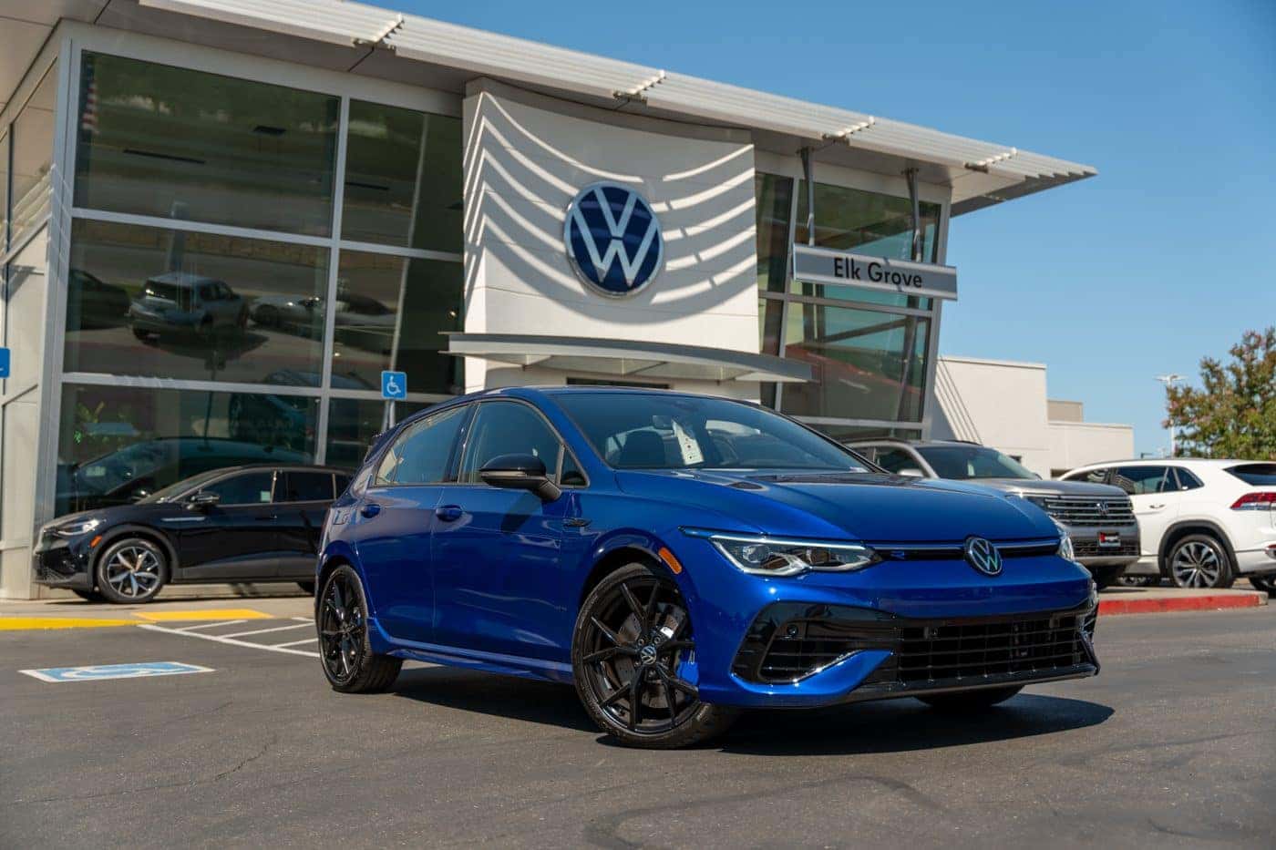 A blue Volkswagen Golf R parked in front of the Elk Grove Volkswagen showroom