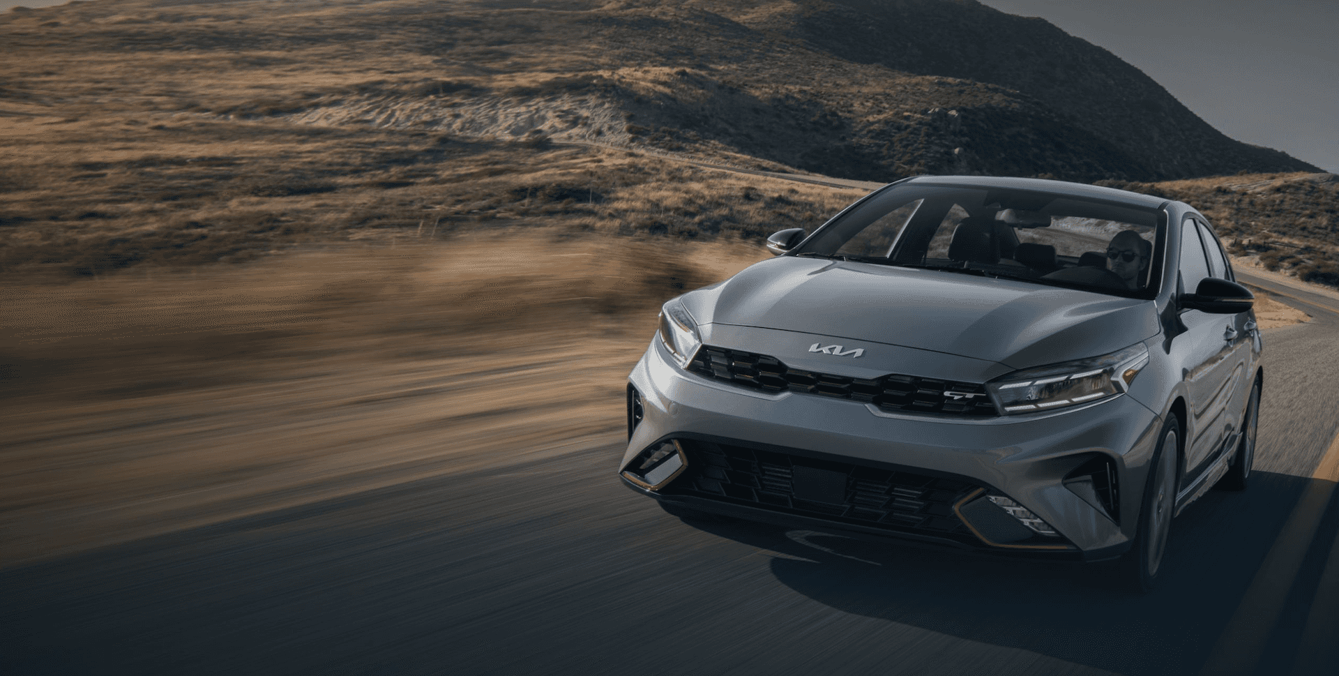 2023 gray Kia Forte driving on a road with mountainous scenery