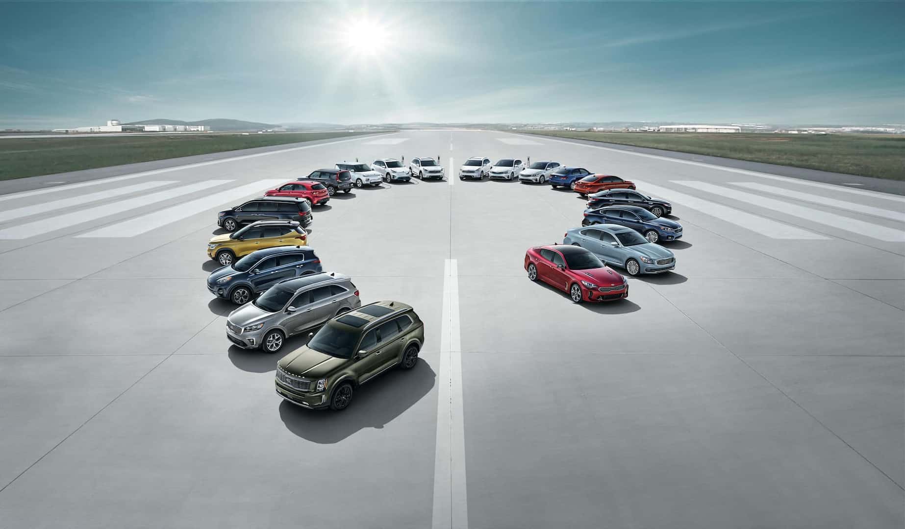 Family photo of Kia vehicles parked in a circle on a runway with buildings in the background. 