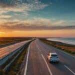 White car driving on an open highway at sunset