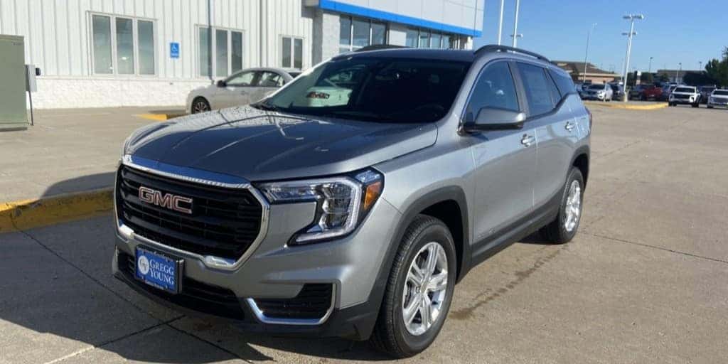 A silver GMC SUV parked in front of a dealership building under a clear blue sky, with a Gregg Young license plate