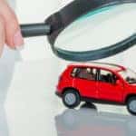 An small SUV underneath a magnifying glass, being inspected for issues which may fall under a Kia warranty.