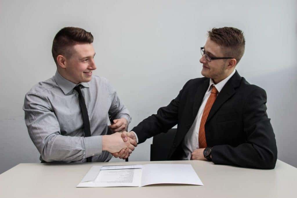 two people shaking hands while smiling inside a dealership