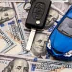 Keys to the car and car that are lying on 100 dollar bills