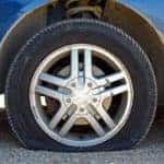 close up of a flat tire of a blue car centered on gravel road