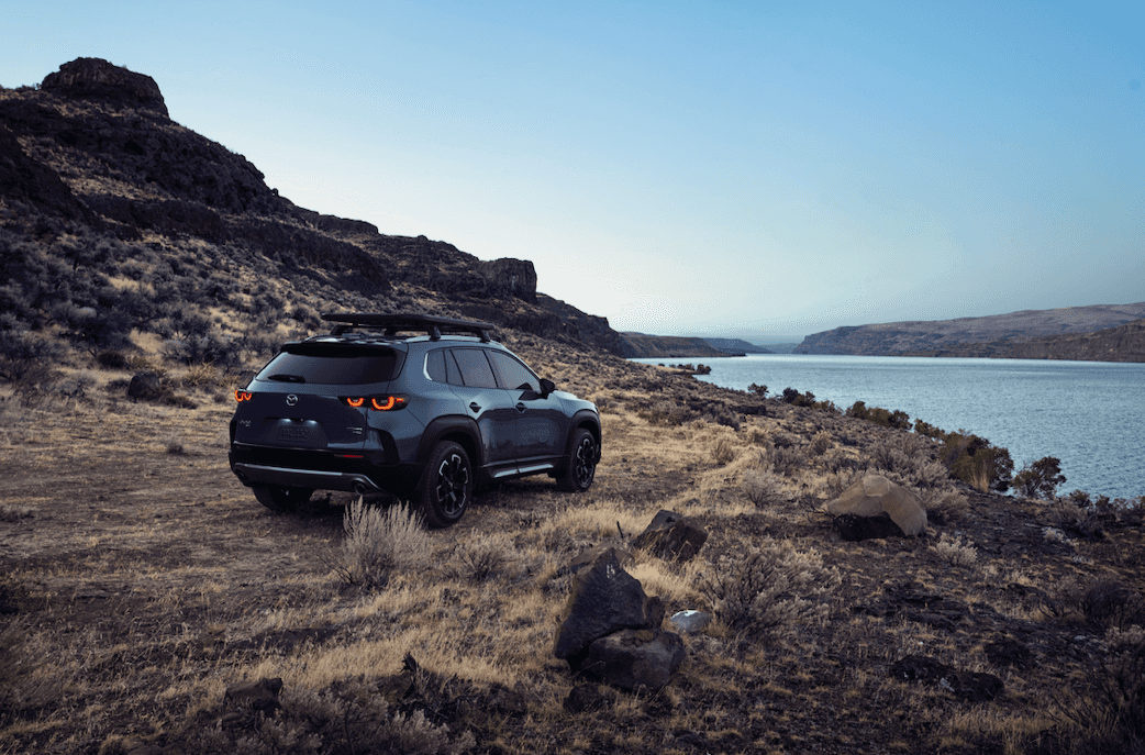 "2023 Mazda CX-50 driving off-road by a body of water."