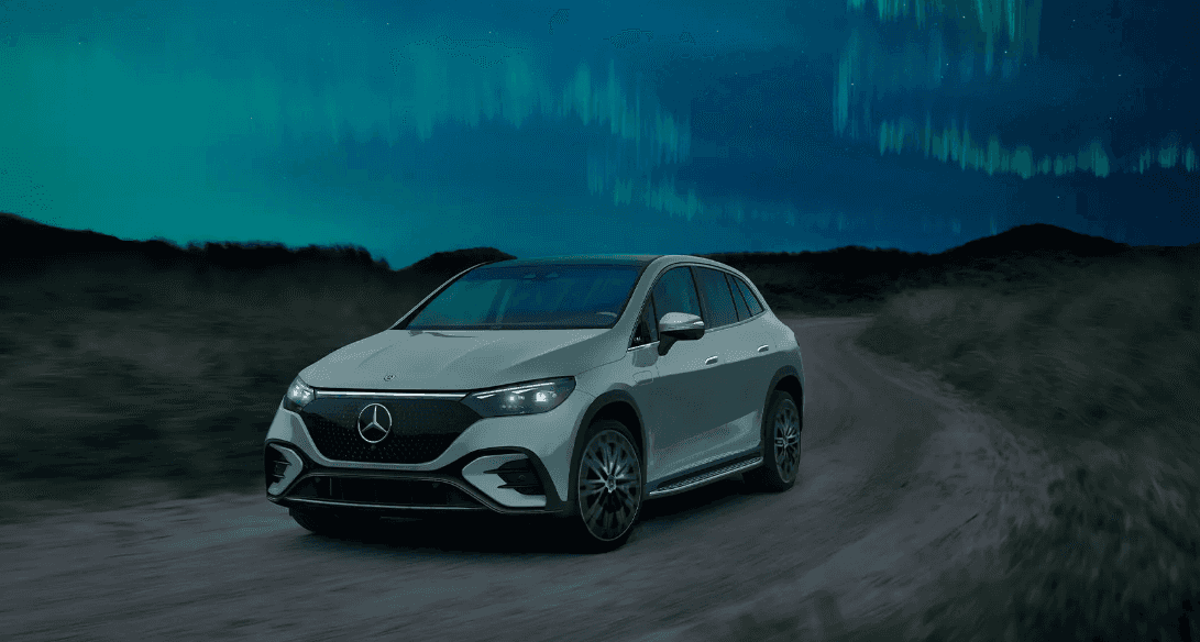 A 2024 Mercedes-Benz EQE SUV drives on a dirt road under an aurora