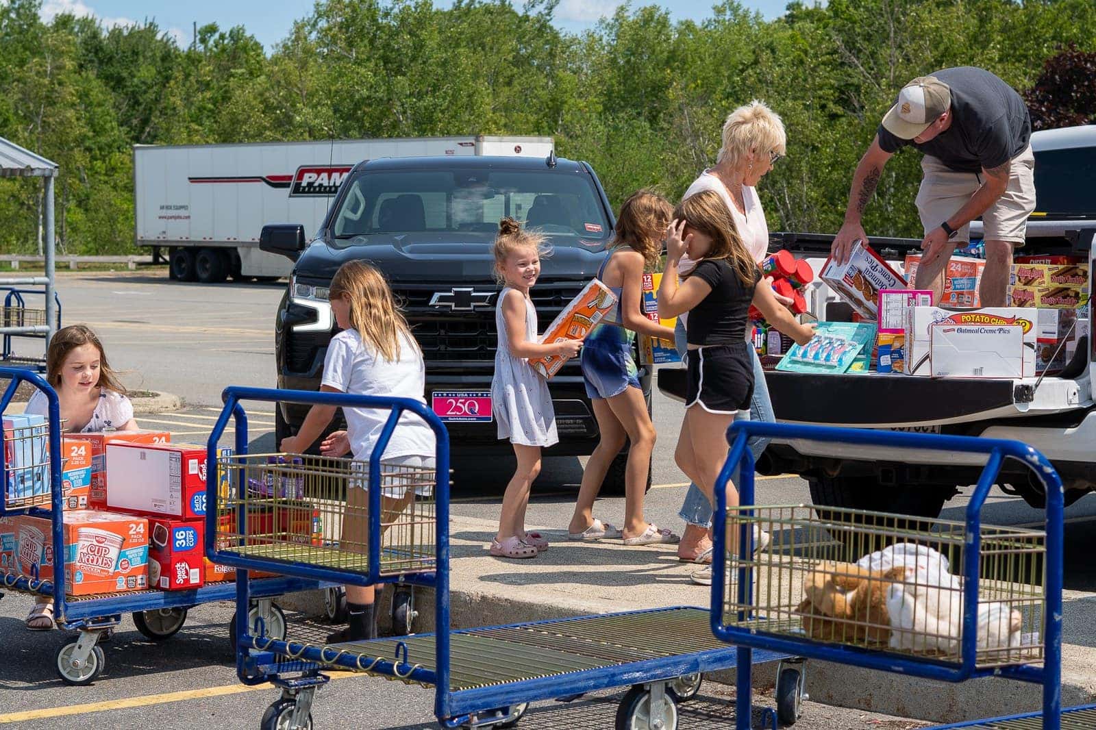 Children and adults moving cases of food from warehouse carts into the back of a pickup truck