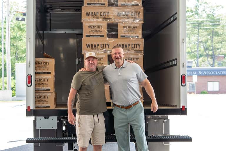 Two men standing together at the back of a box truck loaded with cases of Wrap City kettle chips