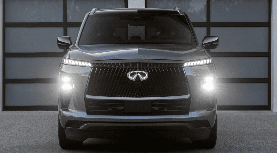 Front three-quarter view of a metallic silver 2026 INFINITI QX80 luxury 3-row SUV displaying an illuminated front emblem, piano-key LED headlights, and ground projection lighting in Ramsey, NJ.