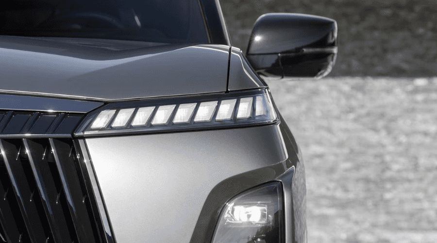 Extreme close-up detail of the 2026 INFINITI QX80 driver side front lighting, showing segmented piano-key LED running lights, lower main headlight projector, dark chrome grille, and side mirror in Bergen County, NJ.