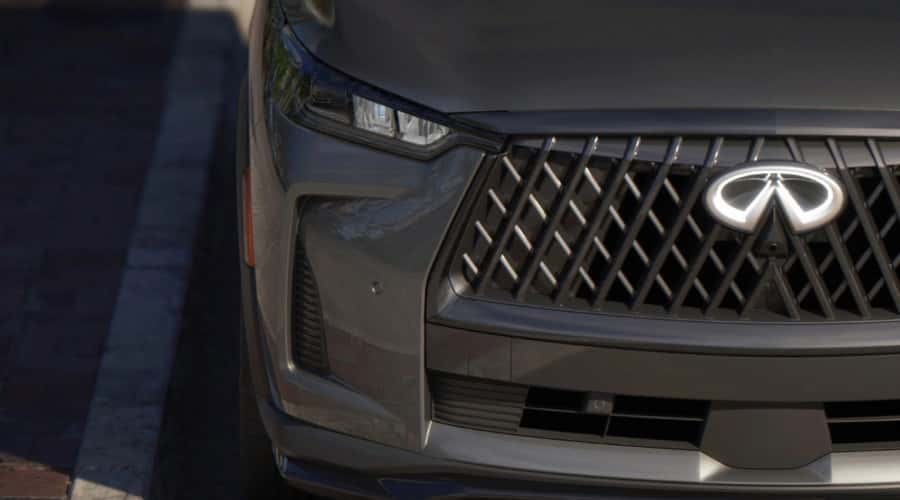Close-up macro view of the front fascia of a 2026 INFINITI QX60 3-row luxury SUV in Harbor Gray featuring the signature illuminated double-arch emblem and mesh grille in Ramsey, NJ.