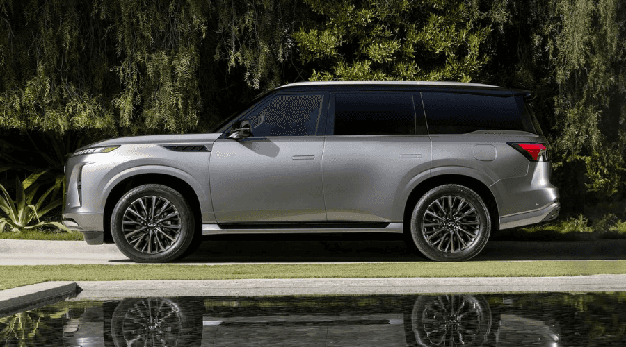 Side profile view of a silver 2026 INFINITI QX80 luxury 3-row SUV parked along a green lawn, showcasing flush door handles, dark alloy wheels, and spacious rear passenger seating equipped with Biometric Cooling in Ramsey, NJ.