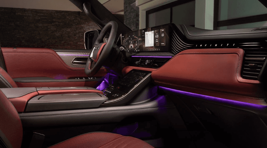 Luxurious front cabin interior of a 2026 INFINITI QX80 showing burgundy leather trim, ambient purple LED strip lighting, dual digital dashboard displays, and climate control touchscreen in Ramsey, NJ.