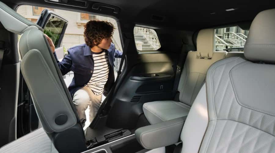 Child stepping through the one-touch tilt and glide second-row seating into the third row of a 2026 INFINITI QX60 3-row luxury SUV in Ramsey, NJ.