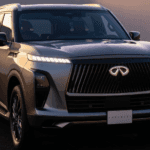 Front three-quarter view of a metallic silver 2026 INFINITI QX80 luxury 3-row SUV displaying an illuminated front emblem, piano-key LED headlights, and ground projection lighting in Ramsey, NJ