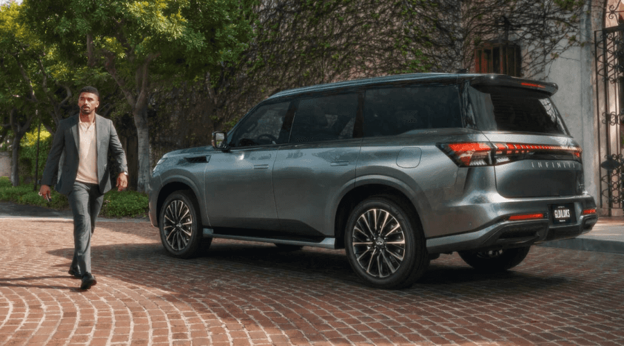 Well-dressed businessman walking toward a dark metallic 2026 INFINITI QX80 luxury SUV parked on a paved driveway in Bergen County near Ramsey NJ