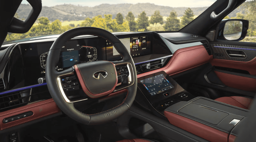 Full dashboard view of the 2026 INFINITI QX80 luxury interior featuring dual 14.3-inch Monolith touchscreen displays, Google built-in navigation, lower HVAC touch panel, and burgundy leather trim at Ramsey INFINITI in Bergen County, NJ.