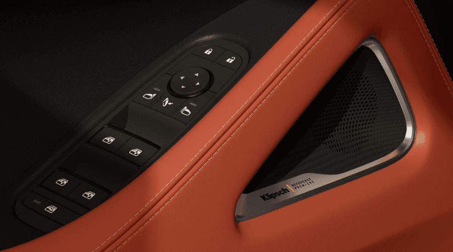 Interior door panel detail of a 2026 INFINITI QX65 featuring burnt orange stitched leather, power window controls, side mirror adjustment buttons, and integrated Klipsch Reference Premiere speaker grille at Ramsey INFINITI in Bergen County, NJ.
