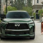 Front view of a deep green 2026 INFINITI QX60 luxury crossover parked on a quiet suburban street in Ramsey, NJ, featuring signature LED headlights and a chrome front grille.