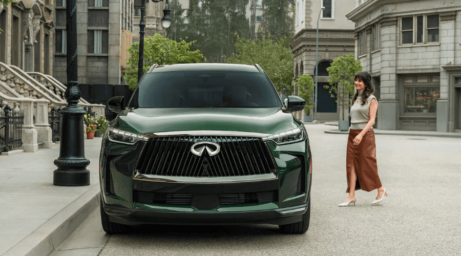 Front view of a deep green 2026 INFINITI QX60 luxury crossover parked on a quiet suburban street in Ramsey, NJ, featuring signature LED headlights and a chrome front grille.
