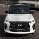 Front view of a white 2026 INFINITI QX80 with black contrast roof featuring an illuminated emblem, LED DRLs, and front camera array for wet weather safety at Ramsey INFINITI near Route 17 in Ramsey, NJ."