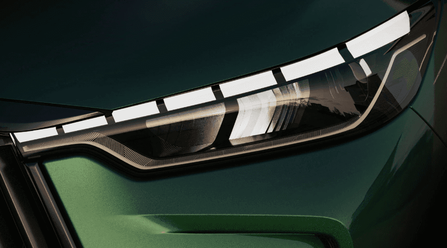 Detailed close-up of the 2026 INFINITI QX60 piano-key LED daytime running lights and headlight housing against deep green metallic paint.