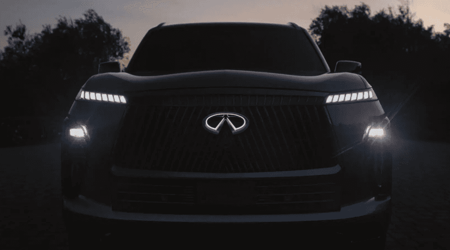 Rear three-quarter view of a white 2026 INFINITI QX80 luxury SUV featuring full-width LED piano-key taillights and black alloy wheels, offering high-visibility wet weather safety at Ramsey INFINITI in Ramsey, NJ.