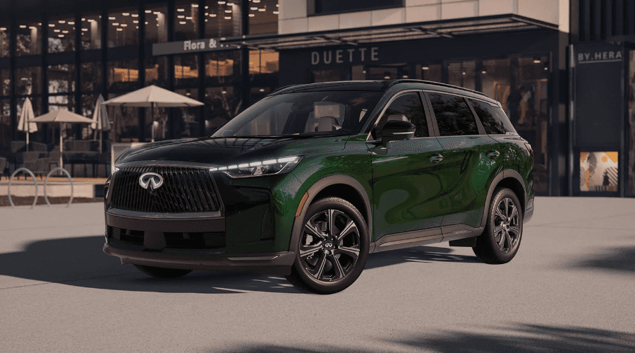 Three-quarter front view of a deep green 2026 INFINITI QX60 luxury crossover parked outside a local shop in Ramsey, NJ, featuring LED headlights and dark alloy wheels.