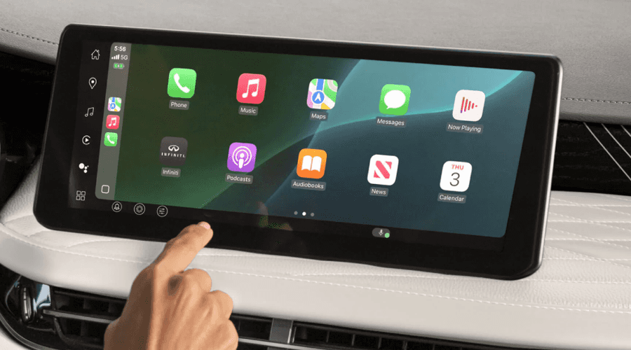 Close-up of a driver operating the widescreen touchscreen infotainment system running Apple CarPlay on the leather-stitched dashboard of a 2026 INFINITI QX60.
