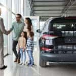 Young happy family shaking hands with a car salesperson in a showroom.