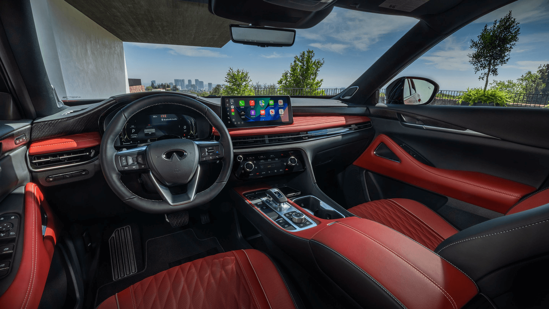 Wide view of the 2027 INFINITI QX65 driver-focused cockpit with red leather seats, digital displays, center console, and panoramic cabin layout.