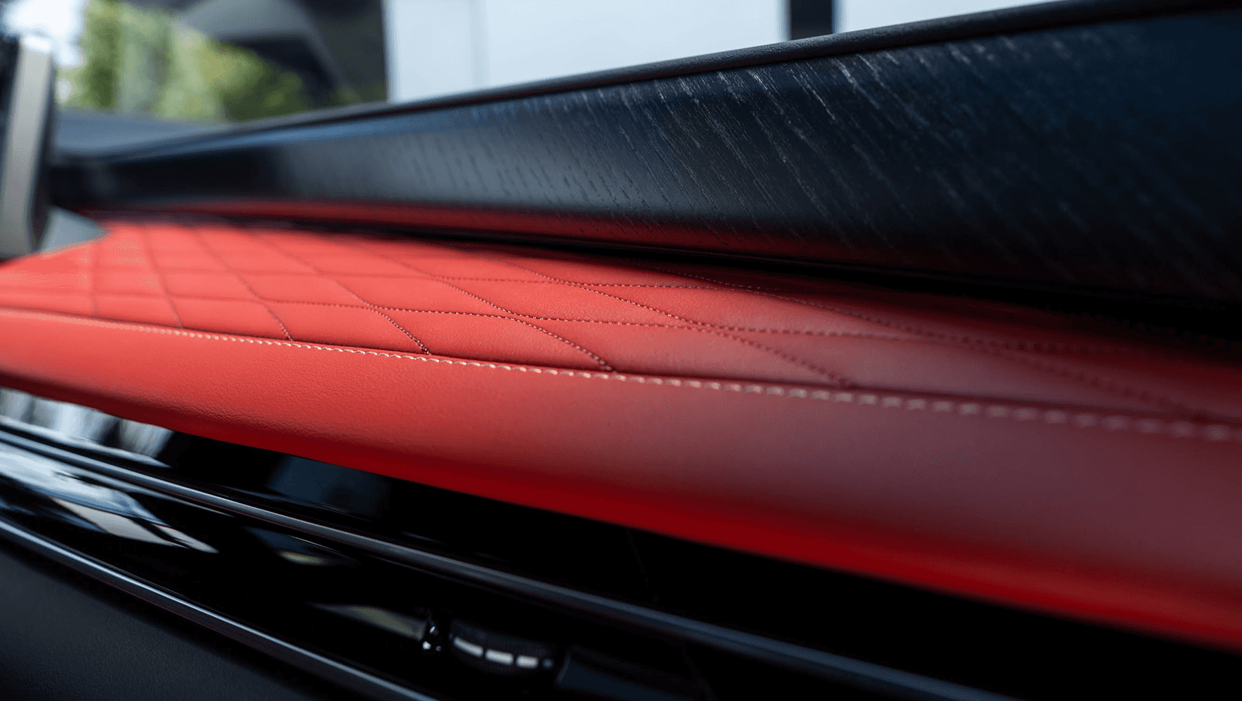 Close-up of the 2027 INFINITI QX65 dashboard with red stitched leather, quilted detailing, dark wood trim, and glossy black accents.
