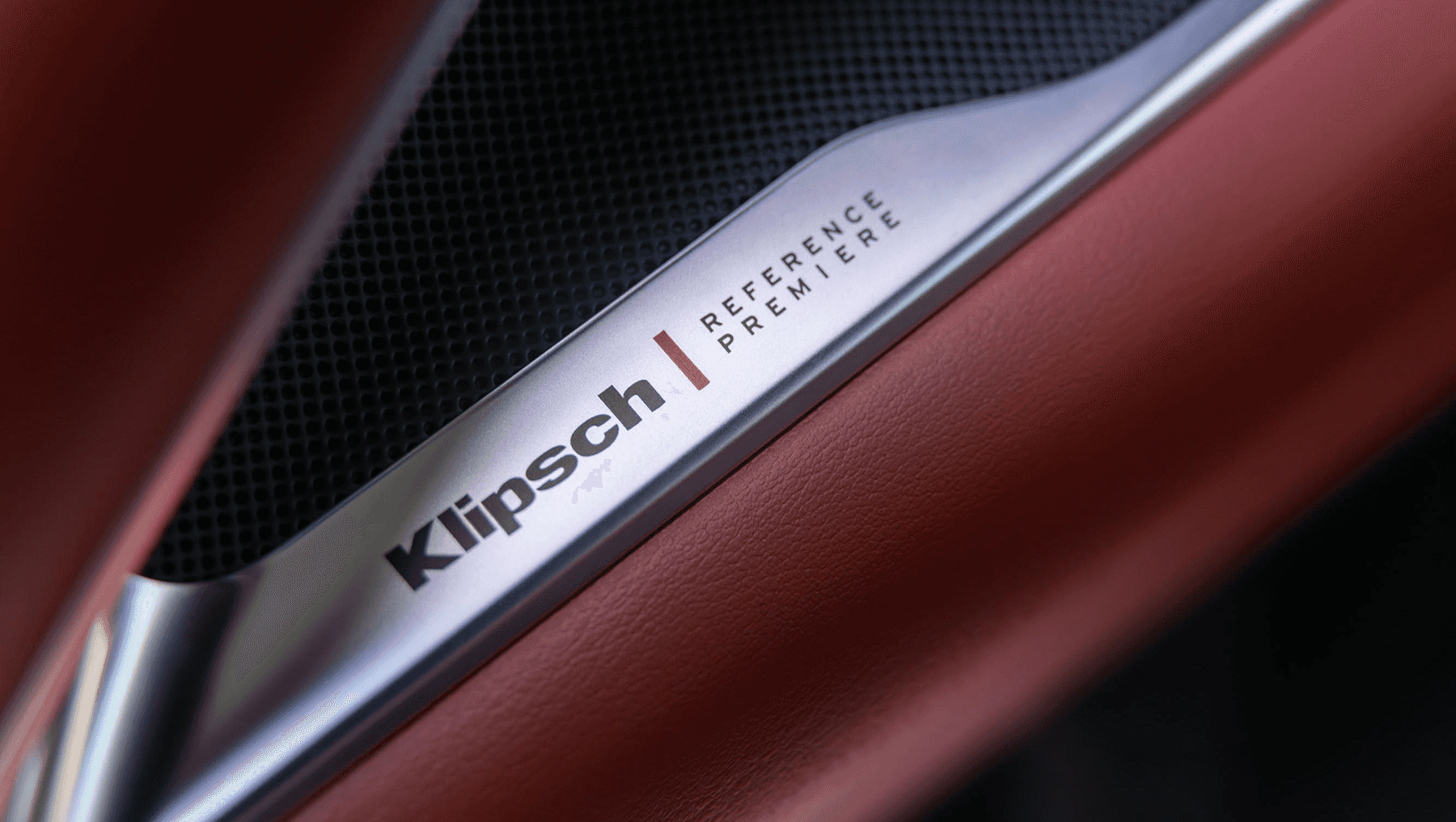 Close-up of the 2027 INFINITI QX65 Klipsch Reference Premiere speaker trim integrated into red leather interior paneling.