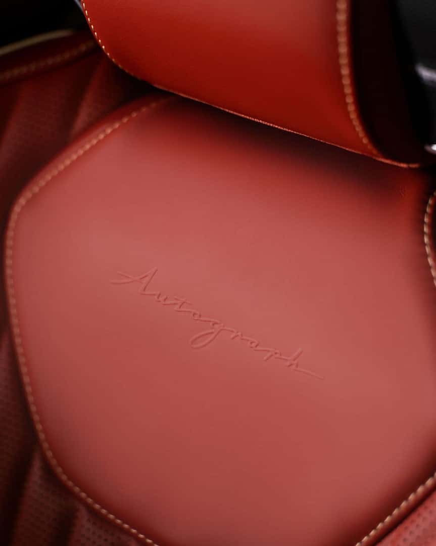 Close-up of the 2027 INFINITI QX65 front seat headrest with embossed Autograph branding on smooth red leather.
