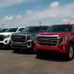 A lineup of GMC cars including SUVs and a red GMC Sierra truck parked in an outdoor lot under a blue sky, showcasing the bold grilles, chrome accents, and signature GMC design.