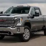 A metallic silver GMC Sierra 2500 heavy-duty pickup truck parked outdoors on pavement, showcasing its bold chrome grille, red GMC badge, and rugged professional-grade design.