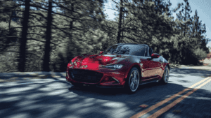 Ruby red 2022 Mazda Miata convertible drives past trees