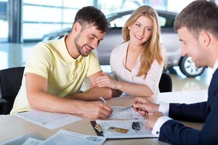 A couple signs paperwork for their used car at a dealership