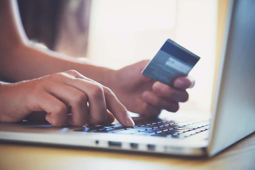 Hand holding credit card beside laptop